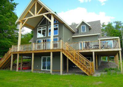 A two-story house with a large wooden deck and stairs on a sunny day.