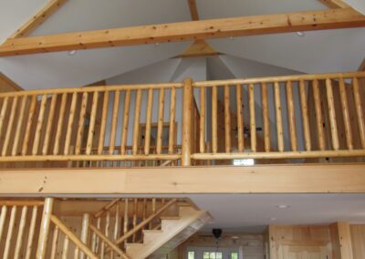 Wooden interior of a home featuring a staircase leading to a loft with a railing, under a high ceiling with a ceiling fan.