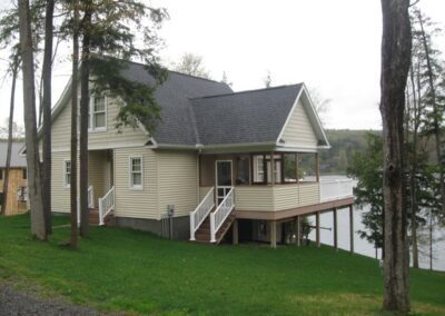 A two-story beige house with white trim featuring a deck that overlooks a body of water.
