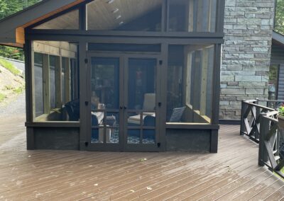 Modern house with a large screened porch and wooden deck surrounded by trees.