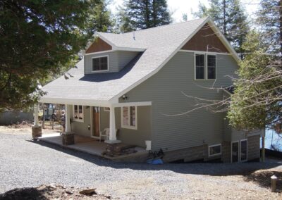 A two-story house with a gray exterior, gabled roof, and a covered front porch surrounded by trees.